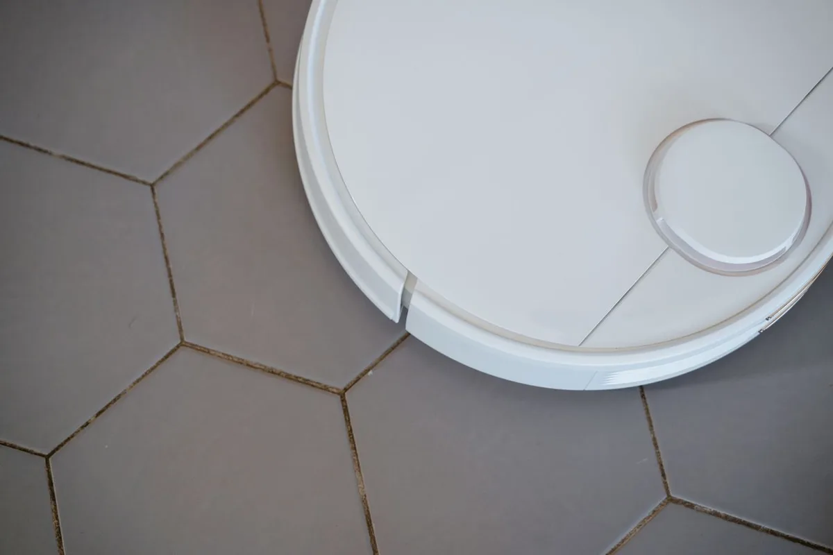 An overhead view of a white robot vacuum on pale floor tiles