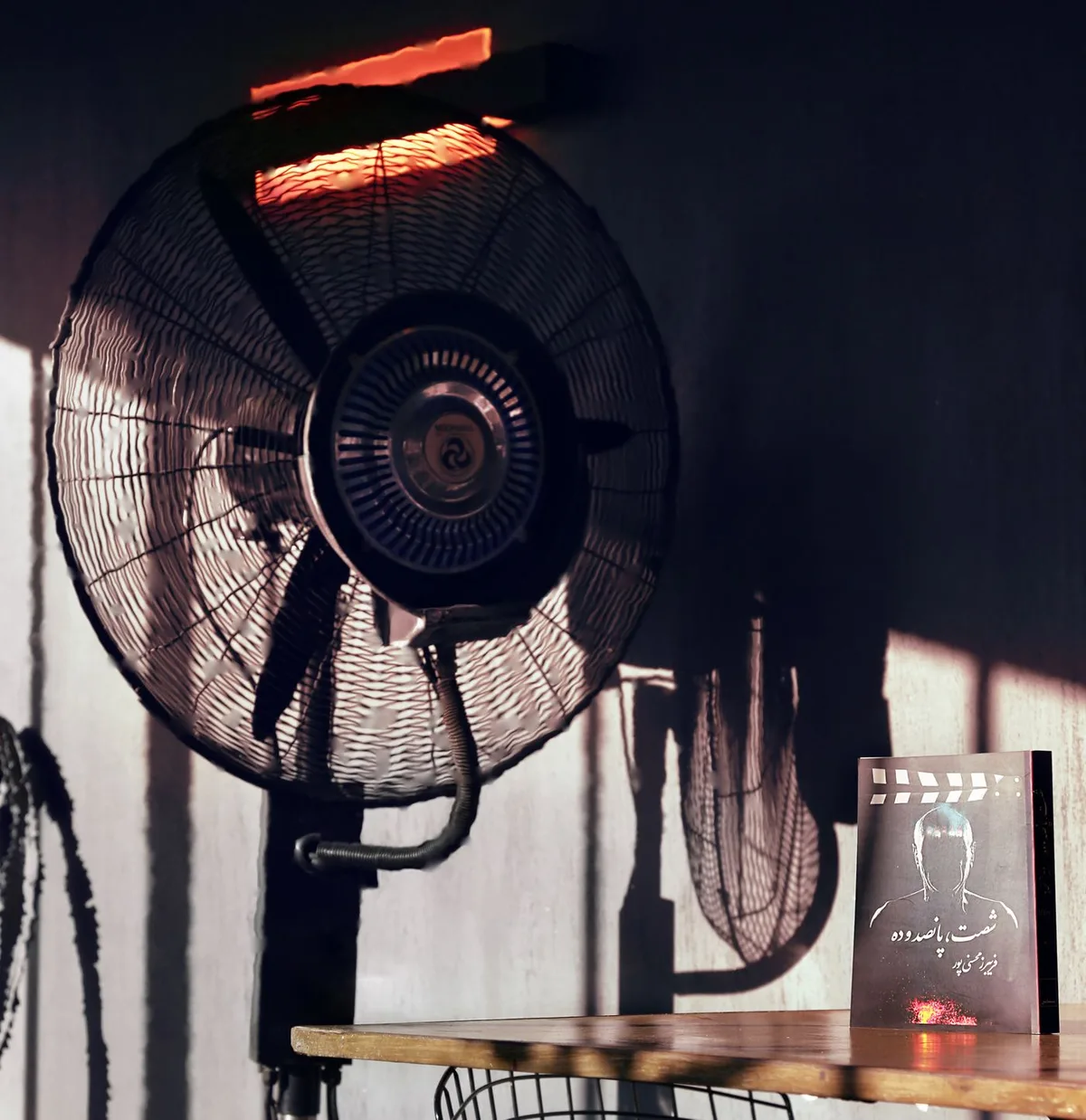 An electric fan beside a book in a sunlit room