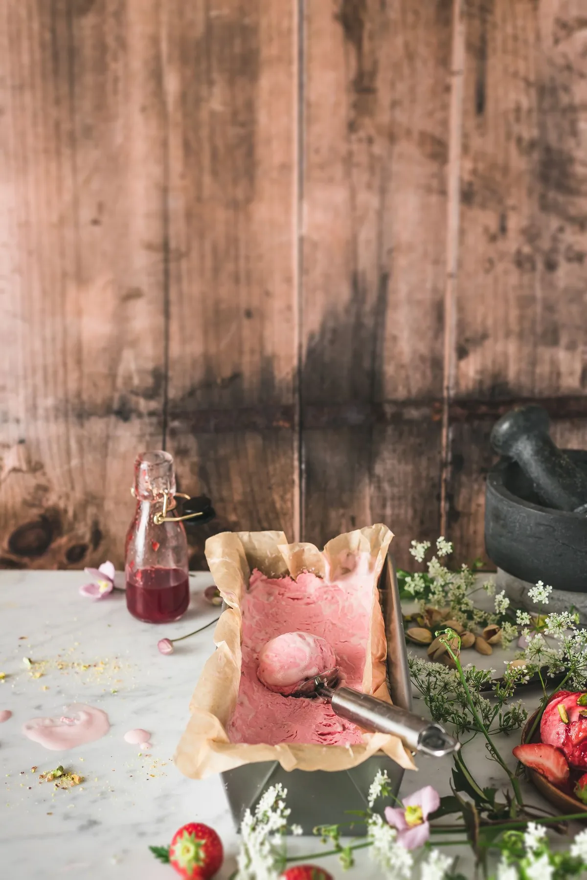 Strawberry ice cream, a scoop, and ingredients on a kitchen table