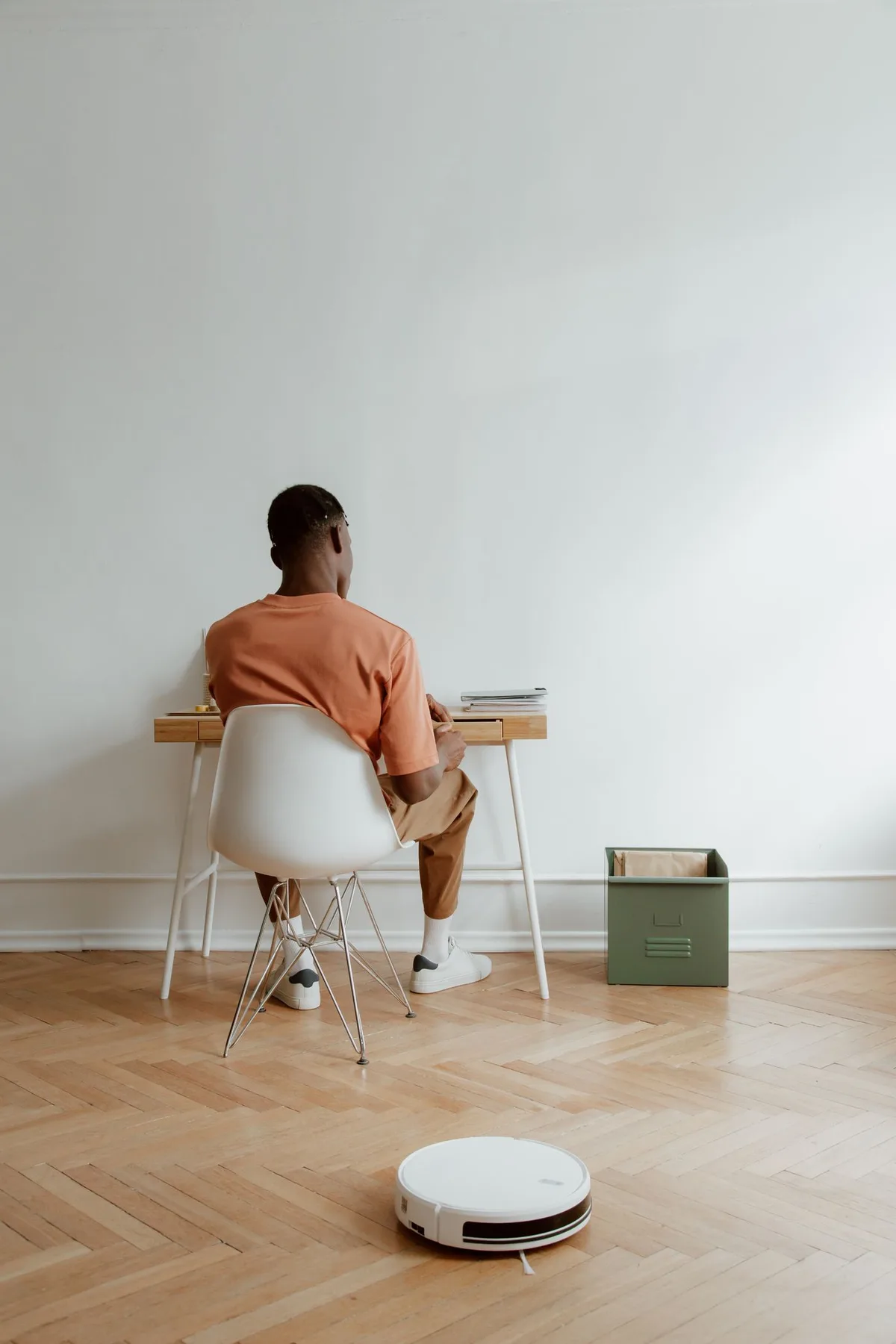 A man working at a desk while a robot vacuum crosses the wooden floor